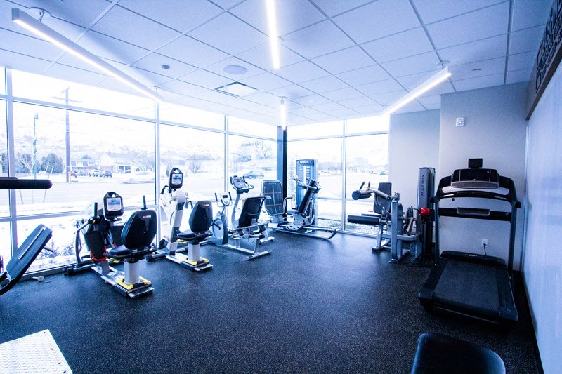 Bright-exercise-room-with-treadmill-stationary-bikes-weight-machines-and-large-windows-overlooking-outdoor-view