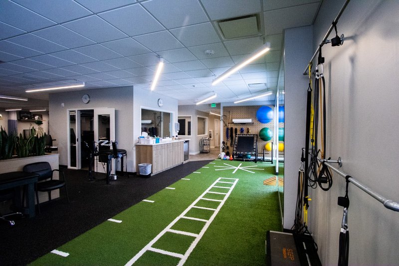 Physical-therapy-training-area-with-green-turf-agility-ladders-exercise-balls-and-suspension-trainers