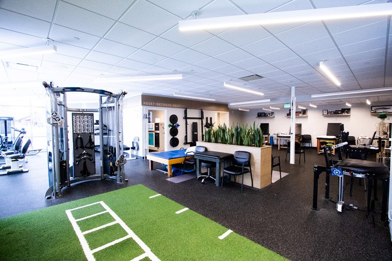 Open-physical-therapy-gym-with-strength-training-equipment-turf-exercise-space-and-patient-treatment-tables